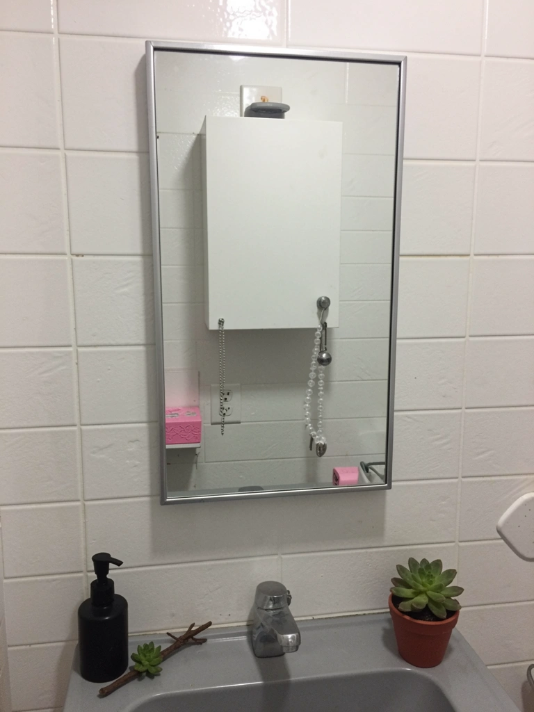 Armário branco instalado acima de uma pia de banheiro, com portas refletindo a luz do ambiente.