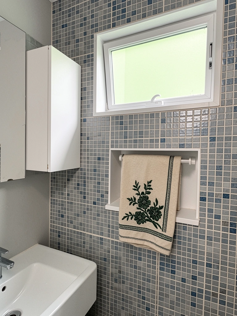 Nichos embutidos na parede do box e armário suspenso sem puxador, azulejos claros e bancada de mármore.