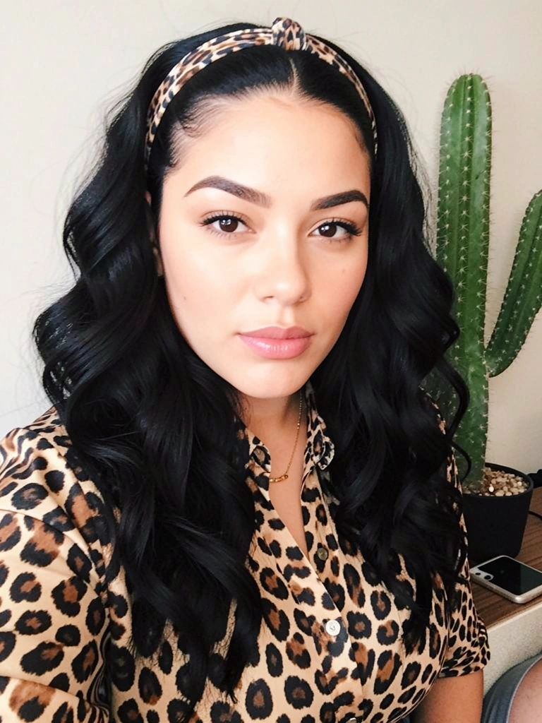 Mulher de cabelos escuros e ondulados usando camisa de estampa de leopardo e faixa de cabeça, com um cacto e um telefone ao fundo.