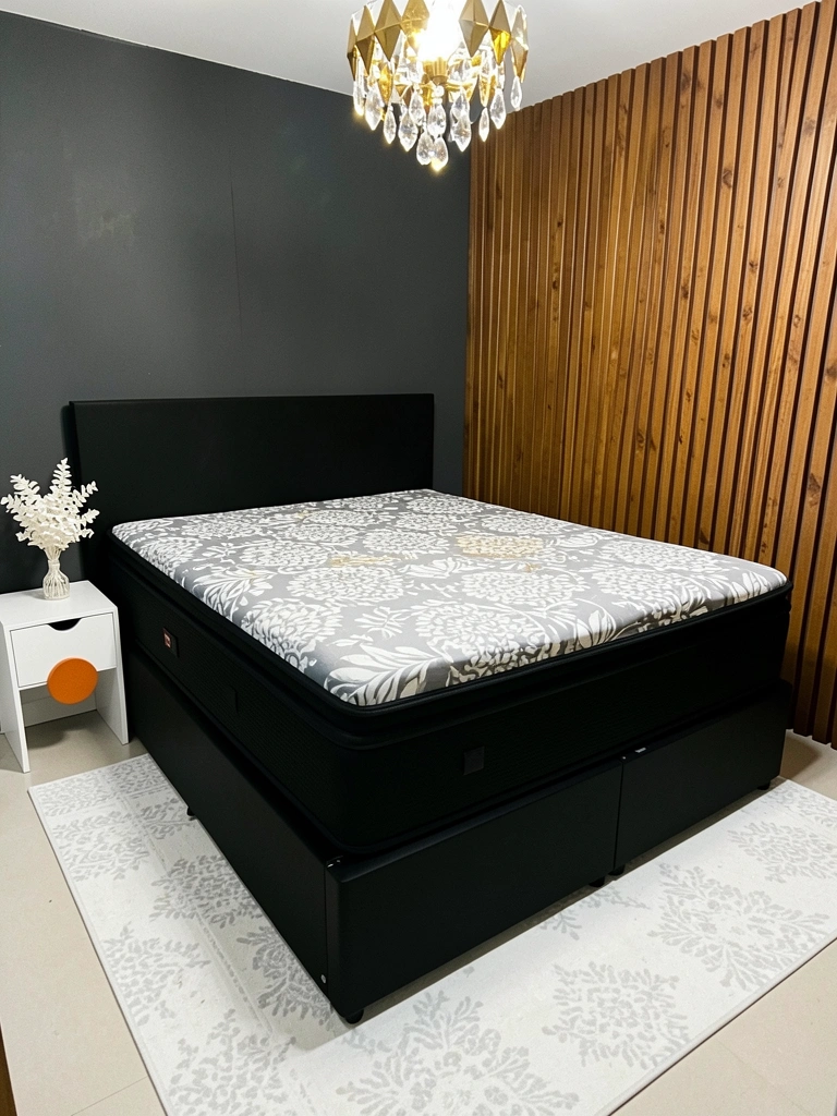 Cama box casal com estrutura estofada e colchão branco, vista frontal em ambiente claro.