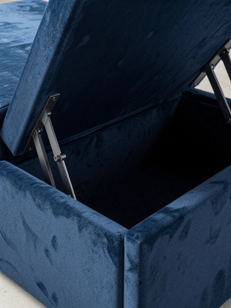 Cama box azul-marinho com mecanismo de abertura revelando compartimento vazio, textura de veludo e detalhes metálicos escovados sob luz suave.