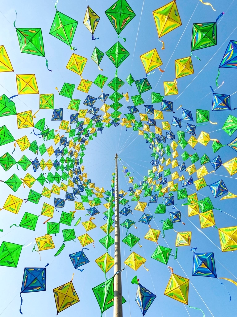 Centenas de pipas coloridas em verde, amarelo e azul formam um vórtice no céu azul claro, com linhas finas se estendendo para cima.