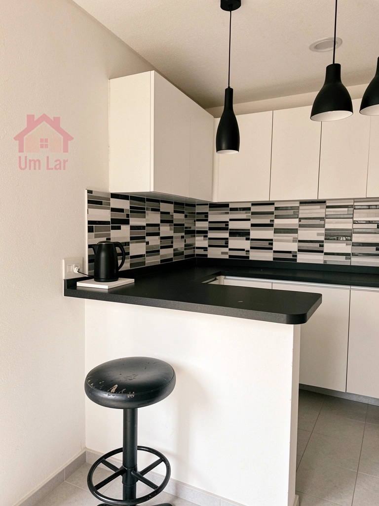 Cozinha americana compacta com bancada e armários claros integrada à sala.