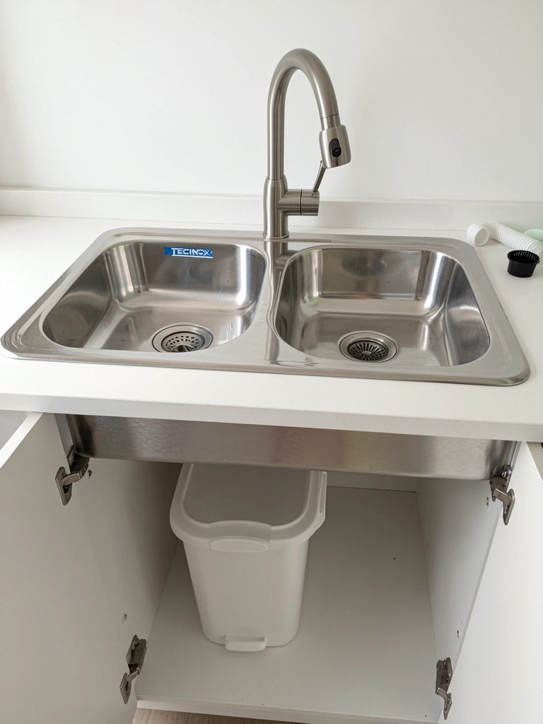 Cuba dupla de aço inox com torneira gourmet e lixeira embutida em bancada de cozinha.