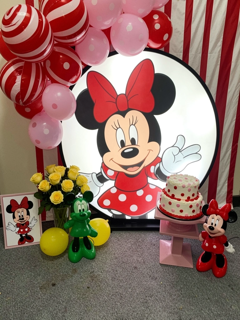 Mesa decorada com toalha vermelha de bolinhas brancas, pratos pretos e detalhes em rosa, fundo com balões vermelhos e pretos.