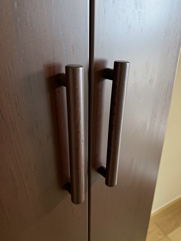 Puxadores cilíndricos de madeira escura fixados em uma porta lisa de tom neutro.