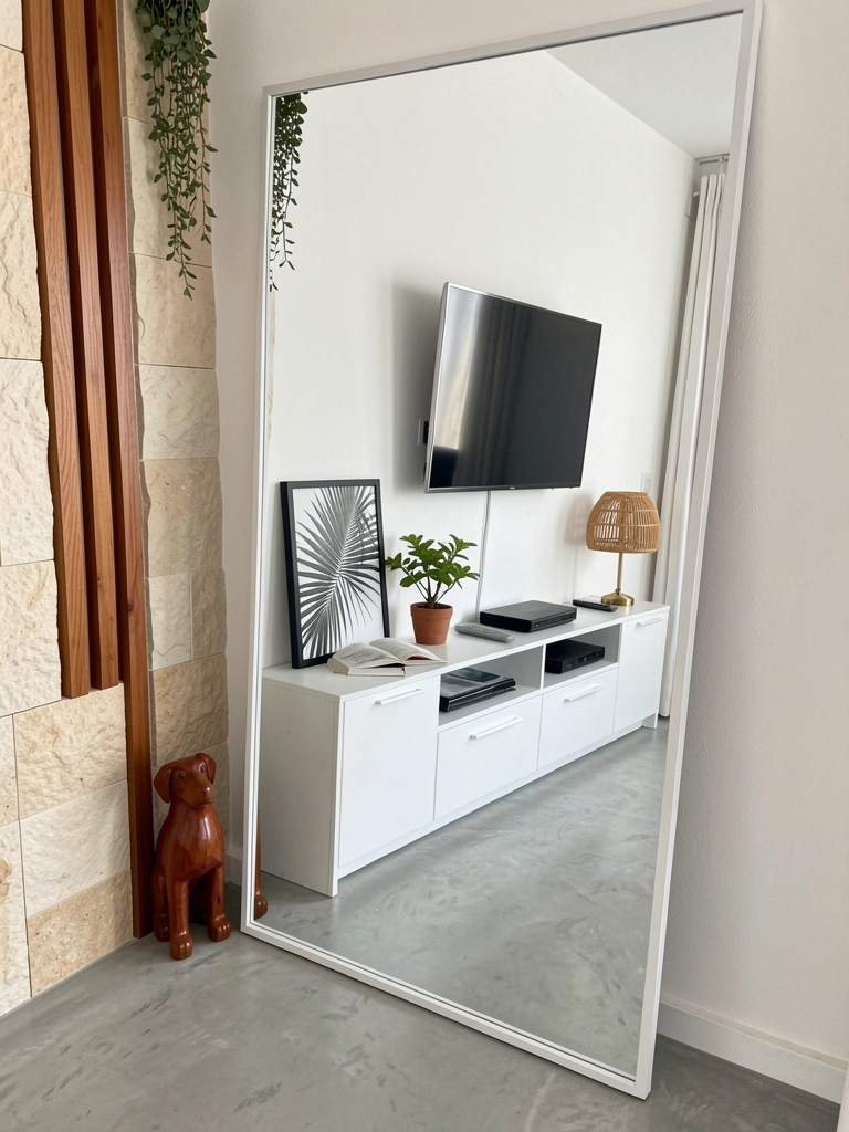 Espelho grande apoiado no chão reflete uma sala com sofá e mesa de centro.