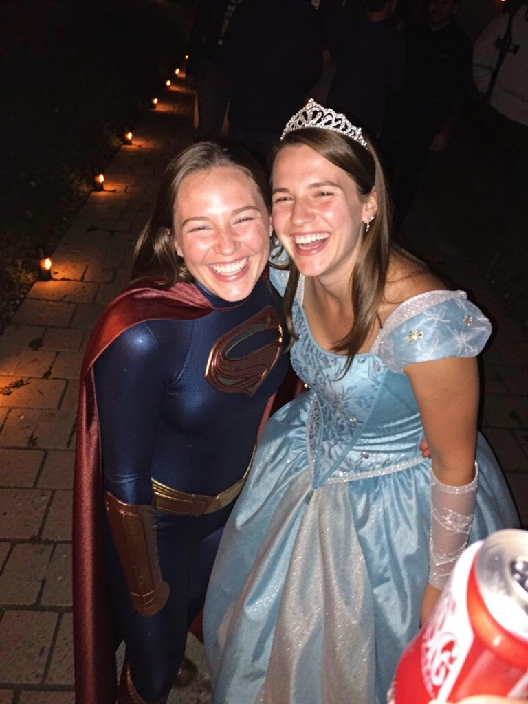 Casal fantasiado: ela de super-herói com capa e máscara, ele de princesa com vestido volumoso e tiara.