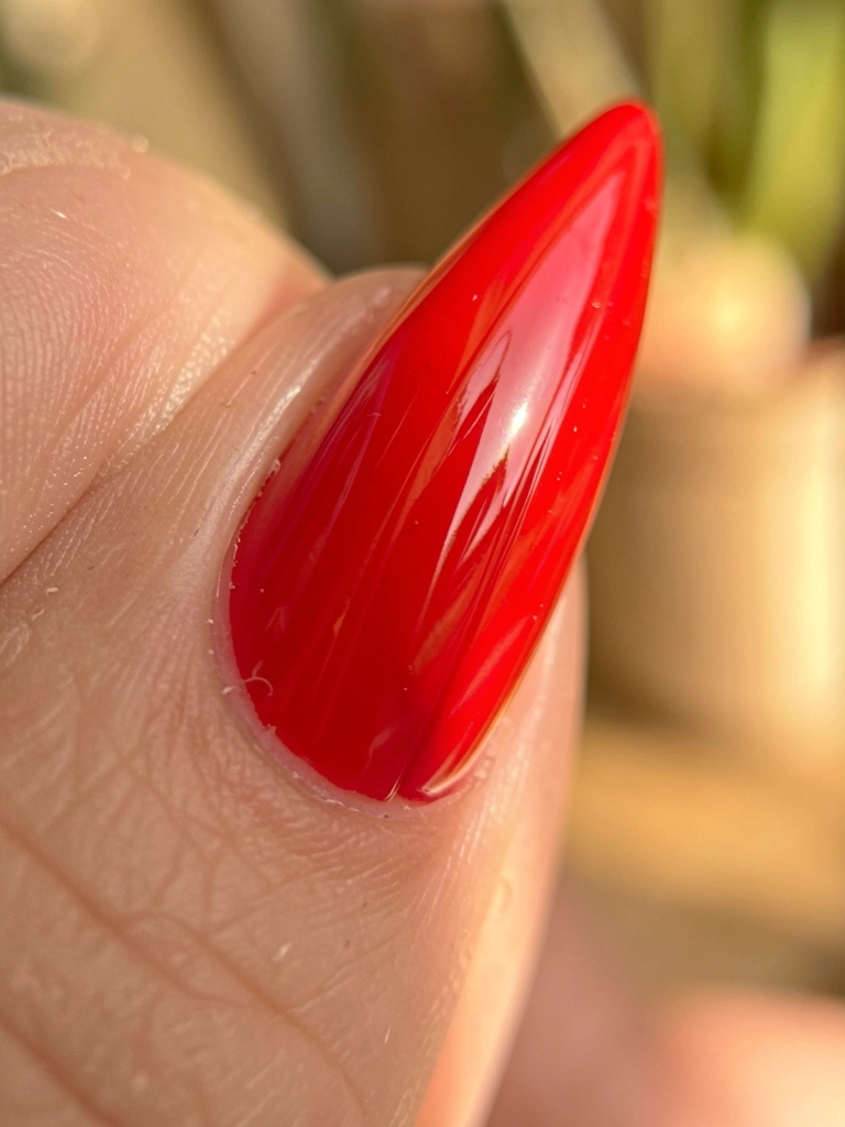 Unha stiletto vermelha vibrante com acabamento espelhado, textura de ranhuras e reflexos sutis, fundo desfocado com luz natural suave.