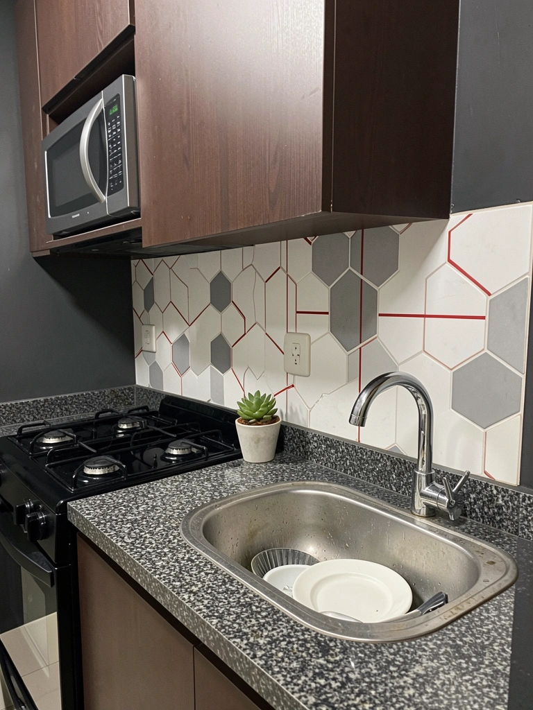 Pia de cozinha com louça empilhada ao lado de parede com papel vinílico estampado, sem danos visíveis.