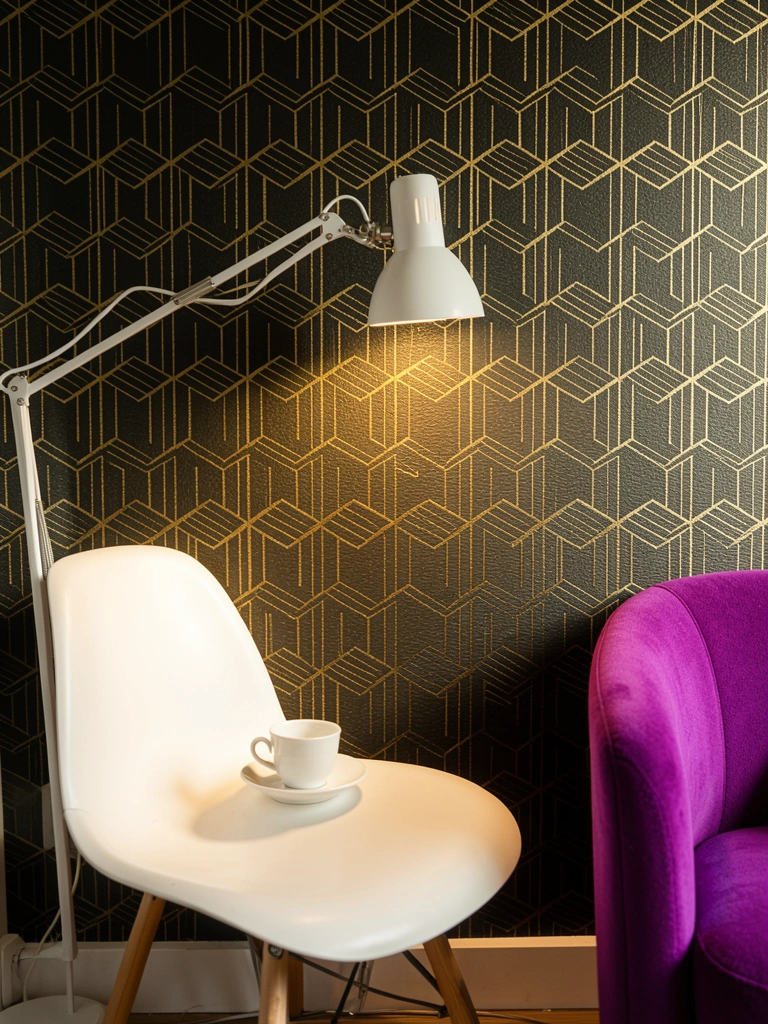 Papel de parede geométrico preto e dourado, luminária de mesa branca sobre cadeira tulipa, poltrona roxa ao lado.