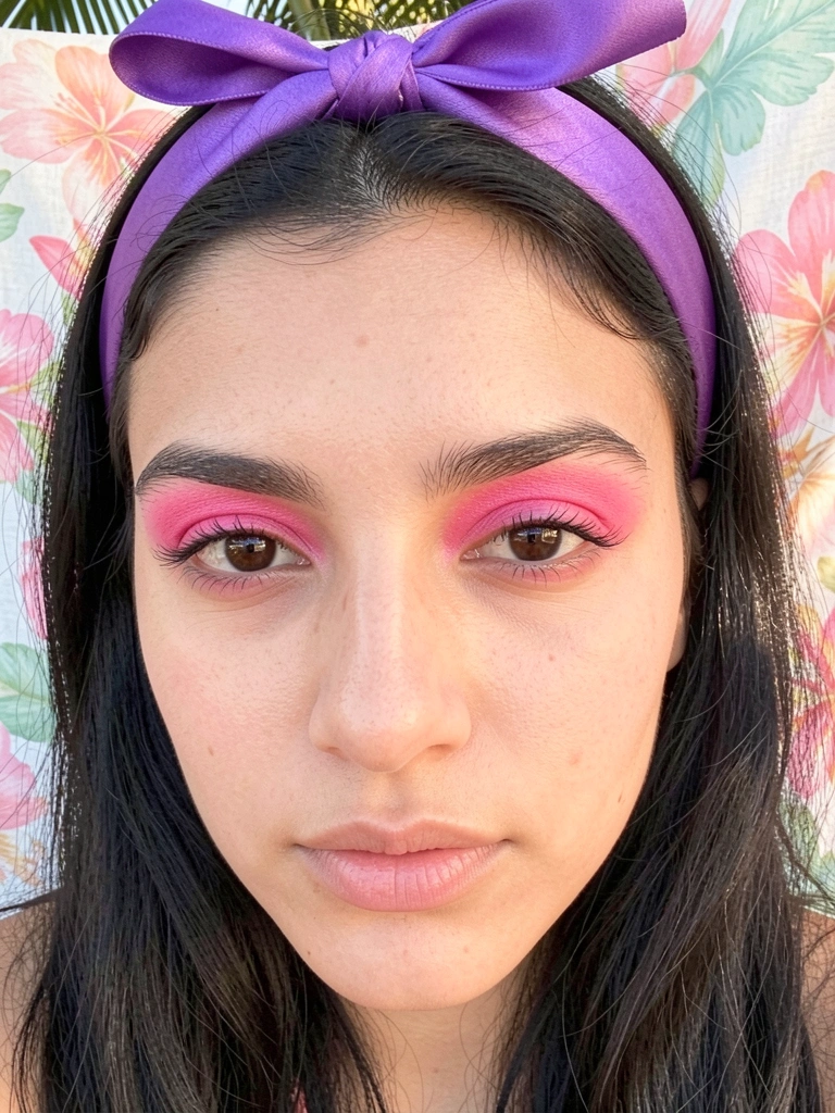 Mulher de cabelo escuro com sombra rosa vibrante e tiara de cetim roxa, luz natural suave e fundo floral pastel.