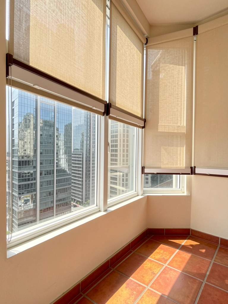 Persiana romana em tecido bege instalada em varanda integrada à sala, com luz natural filtrada.