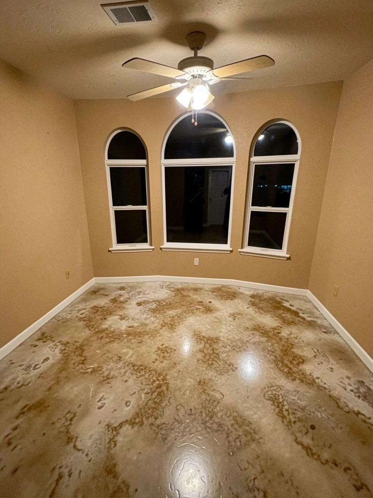 Sala ampla com piso líquido cinza polido, sofá bege e parede de vidro com vista para jardim.