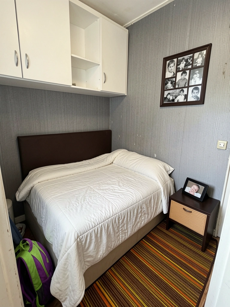 Quarto pequeno com cama de solteiro, guarda-roupa simples e parede sem revestimento.