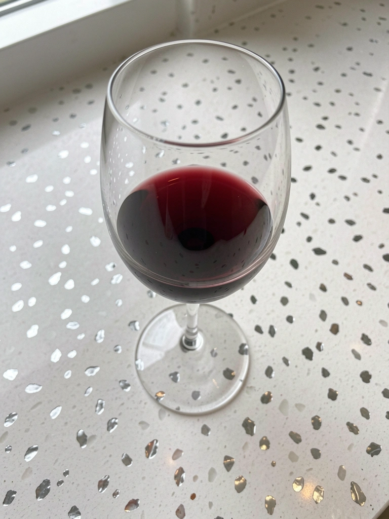 Copo de vinho tinto sobre bancada de quartzo branco, com luz natural incidindo lateralmente.