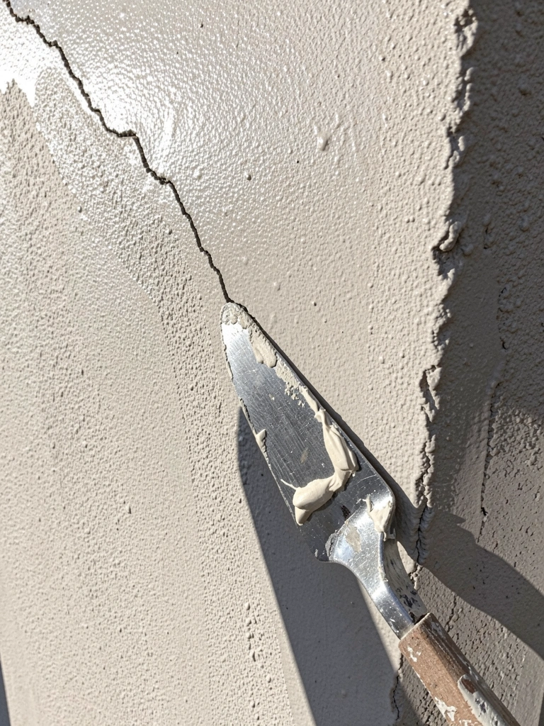 Parede de reboco com fissura visível e espátula com massa ao lado.