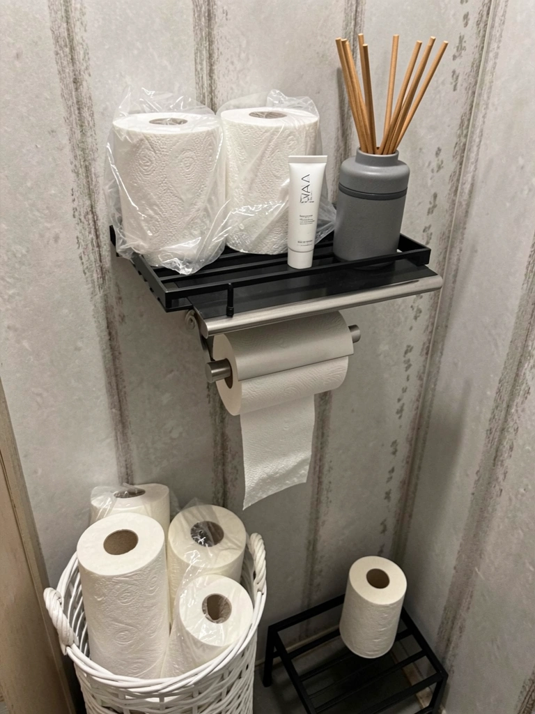 Suportes de papel higiênico de parede, chão e com prateleira em banheiro claro.