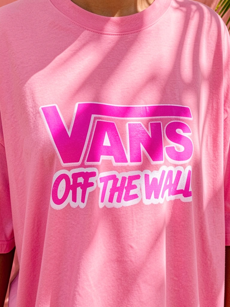 Camiseta rosa Vans com estampa grafite branca e rosa, tecido macio, fundo desfocado com luz solar tropical.