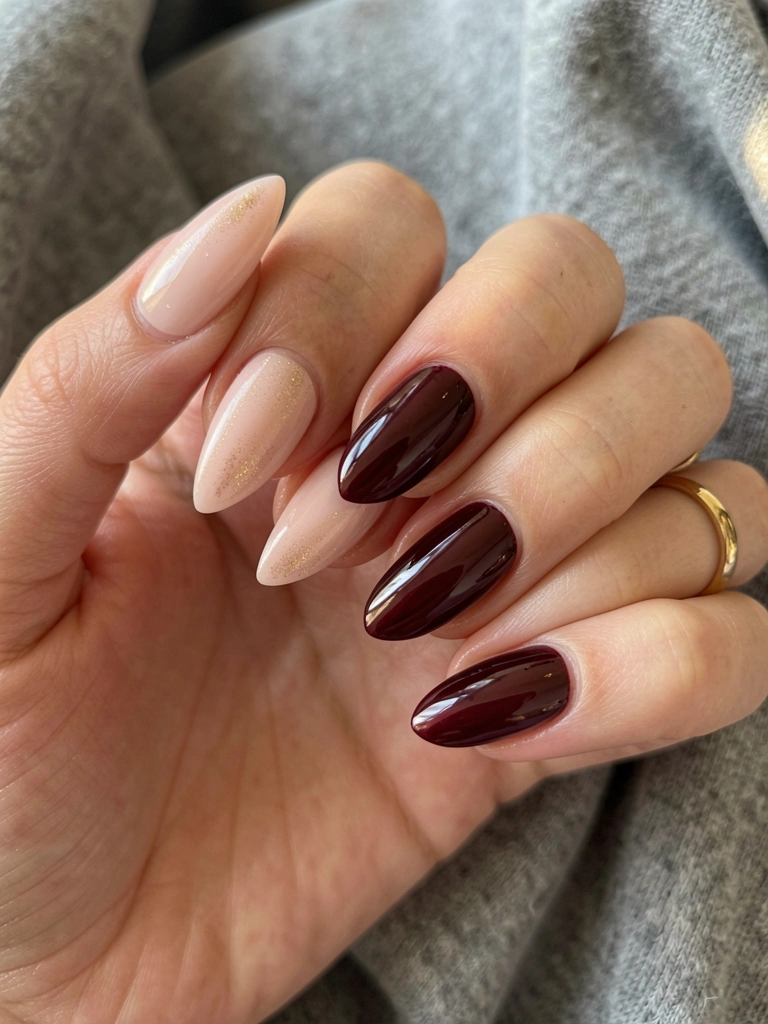 Mãos com unhas em gel rosa claro e shimmer dourado na esquerda e vinho glossy na direita, anel de ouro no dedo anelar, fundo cinza texturizado.