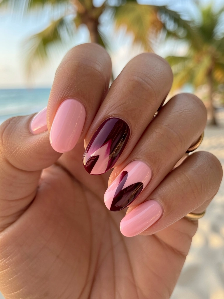 Mão feminina com unhas em degradê rosa e vinho, formato de coração assimétrico, anel de ouro no dedo anelar, fundo desfocado com luz natural.