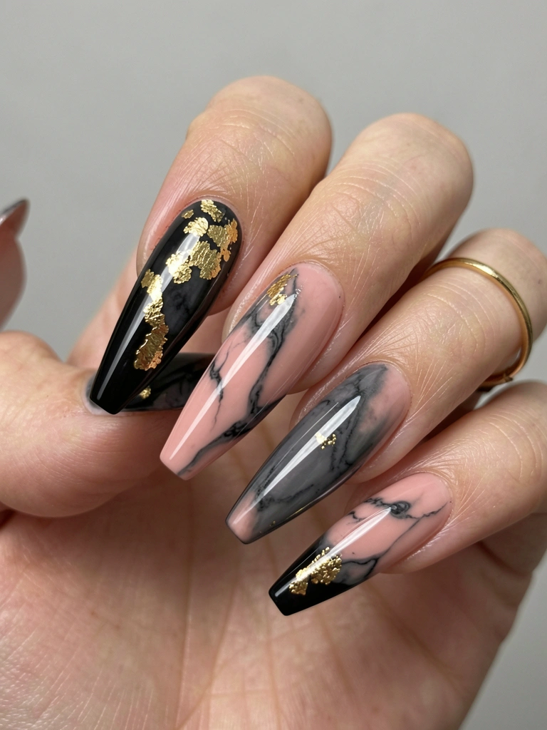 Close-up de unhas acrílicas longas e pretas com folhas de ouro e efeito marmorizado do rosa ao cinza, anel fino no indicador, fundo cinza neutro.