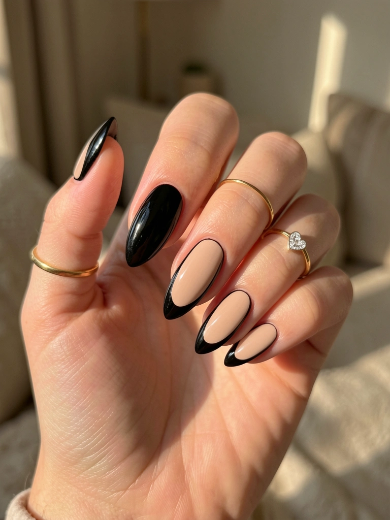 Mão com unhas pretas e nude em formato amendoado, anel de ouro e coração de diamante, luz natural suave e fundo neutro desfocado.