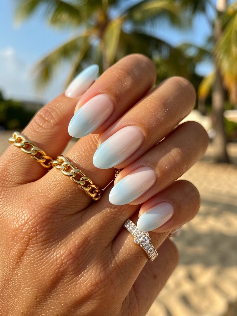 Mão feminina com unhas francesinhas azul claro e branco, efeito ombre, anel de corrente dourada e aliança de diamantes, luz natural