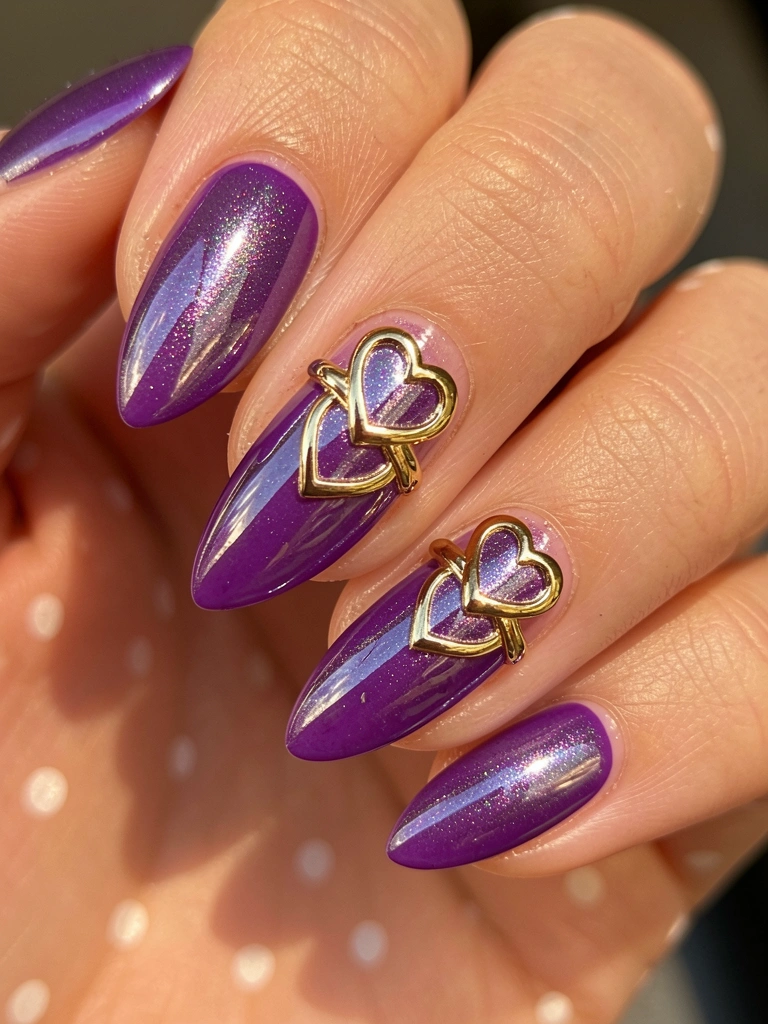 Mão com unhas em formato amendoado e esmalte roxo brilhante, anel dourado em formato de coração, luz natural e fundo desfocado.