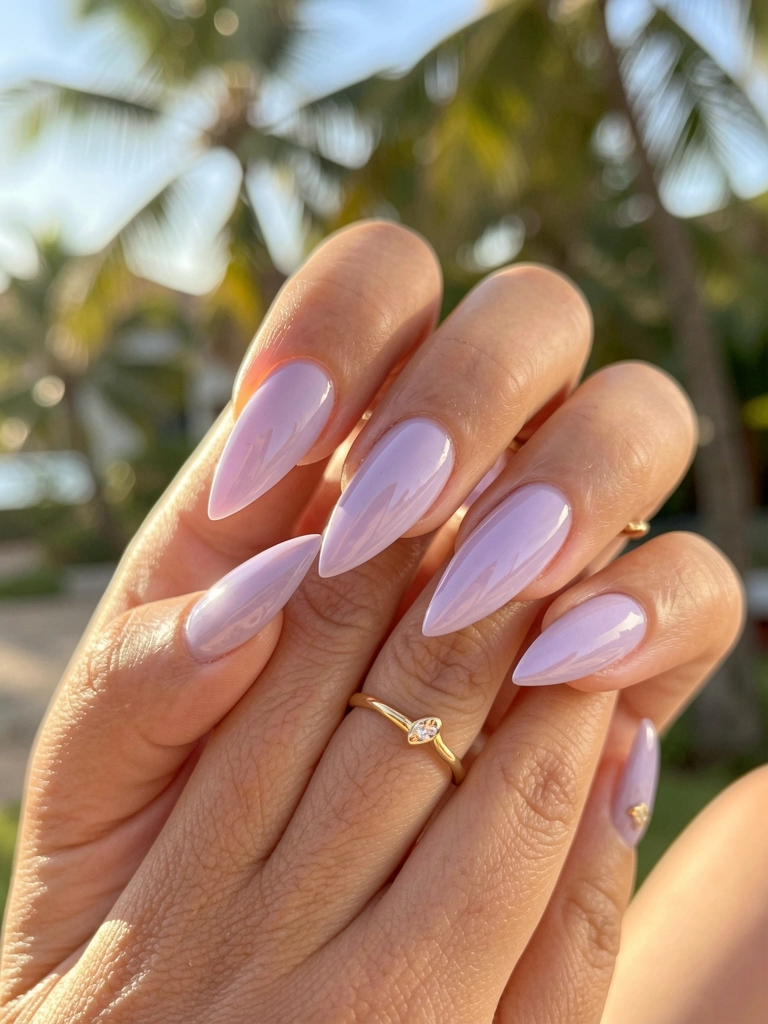 Mãos femininas com unhas lavanda em formato amendoado e acabamento glossy, anel dourado, luz natural suave e fundo desfocado com sugestão de área externa.