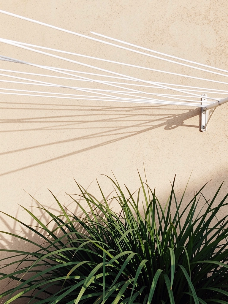 Varal branco esticado em parede bege texturizada, com capim ornamental verde-escuro na frente, luz natural do dia.
