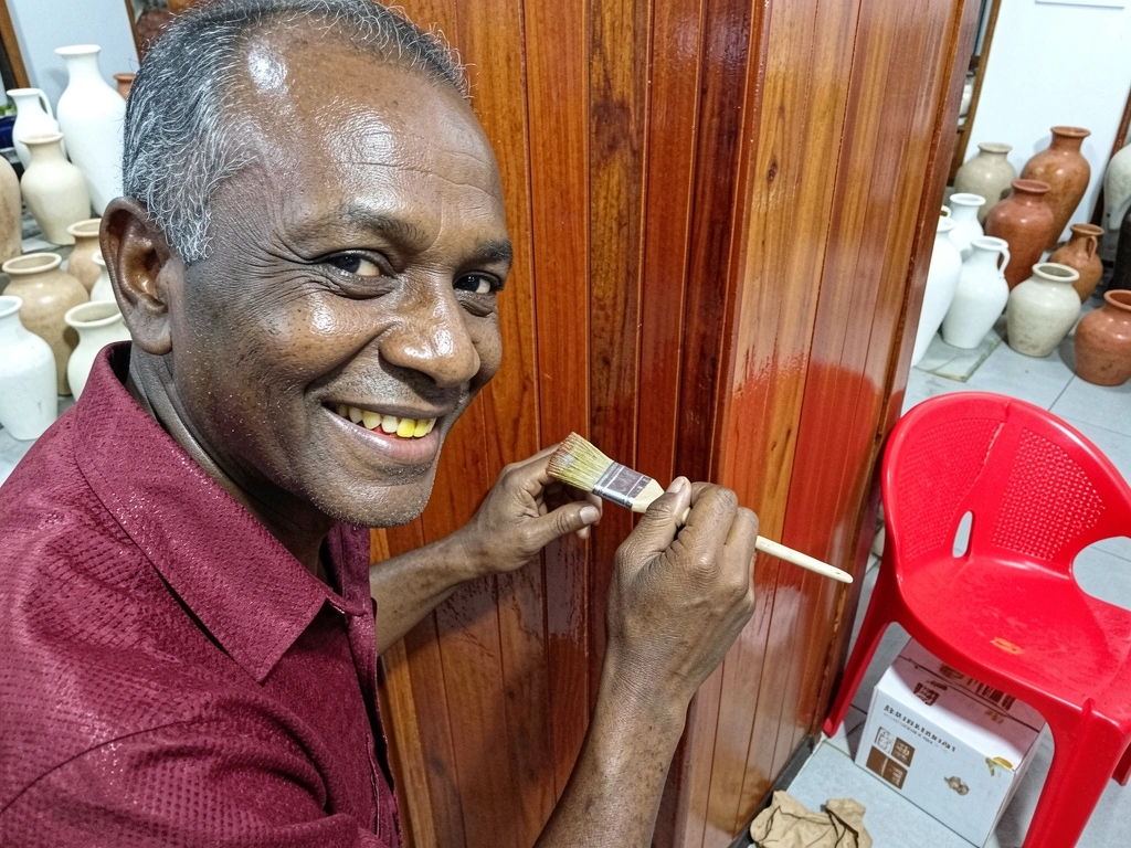 Mão segurando pincel aplicando verniz sobre superfície de madeira.