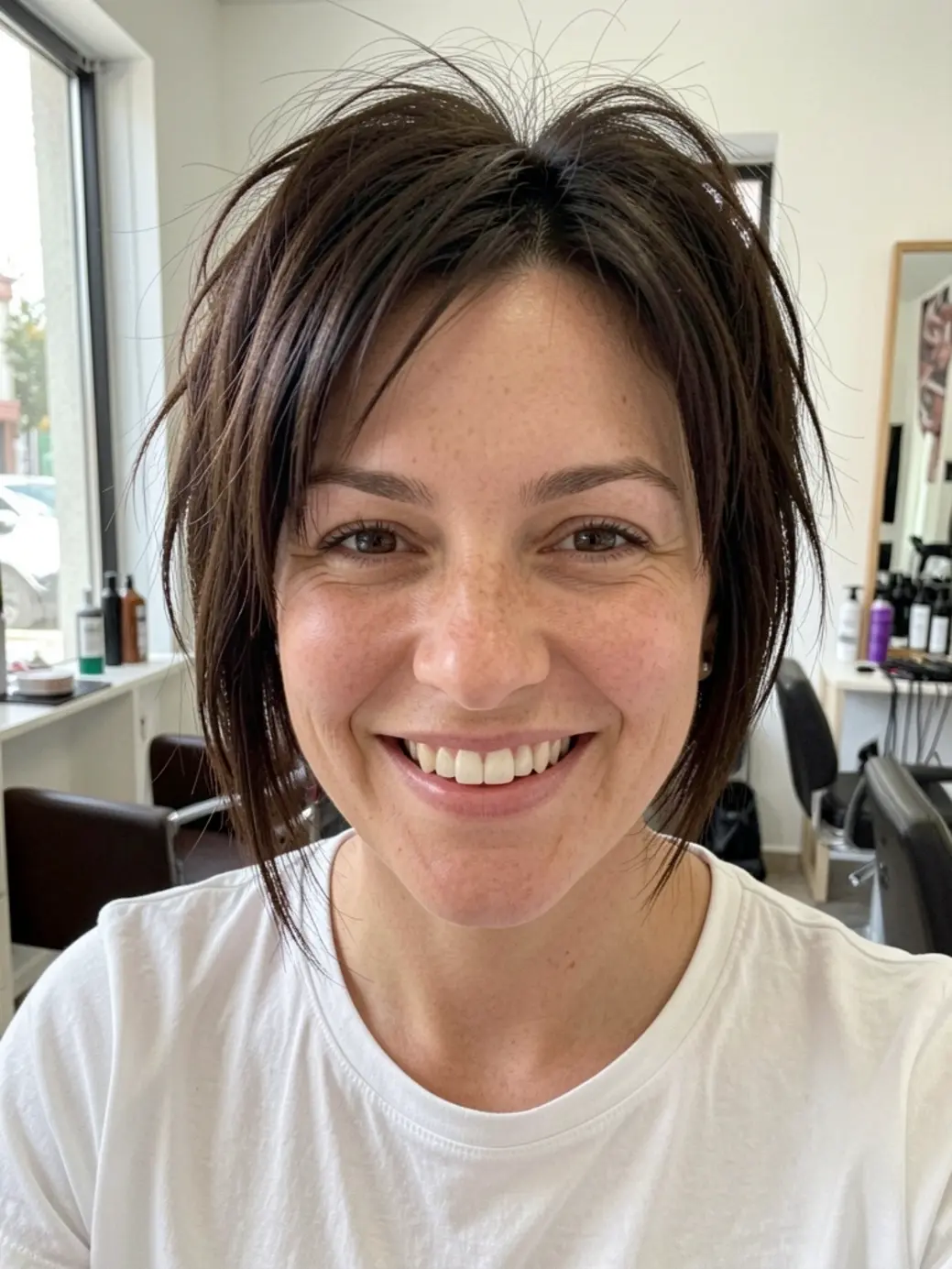 Mulher de cabelo castanho escuro em corte V com camadas desconexas, sorriso natural, pele com sardas, luz de janela.