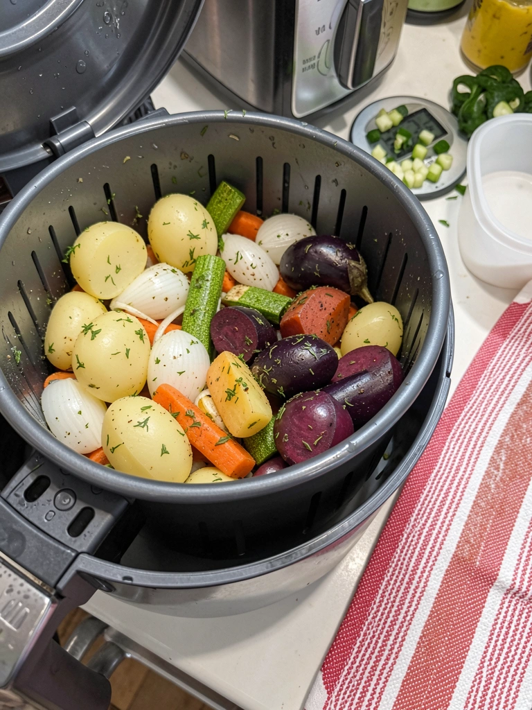Relógio de cozinha ao lado de uma airfryer, com legumes cortados sobre a bancada.