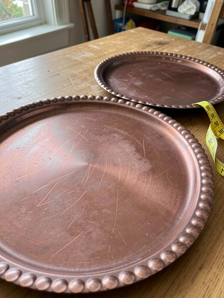 Duas bases redondas de tamanhos diferentes sobre uma mesa, com fita métrica ao lado.