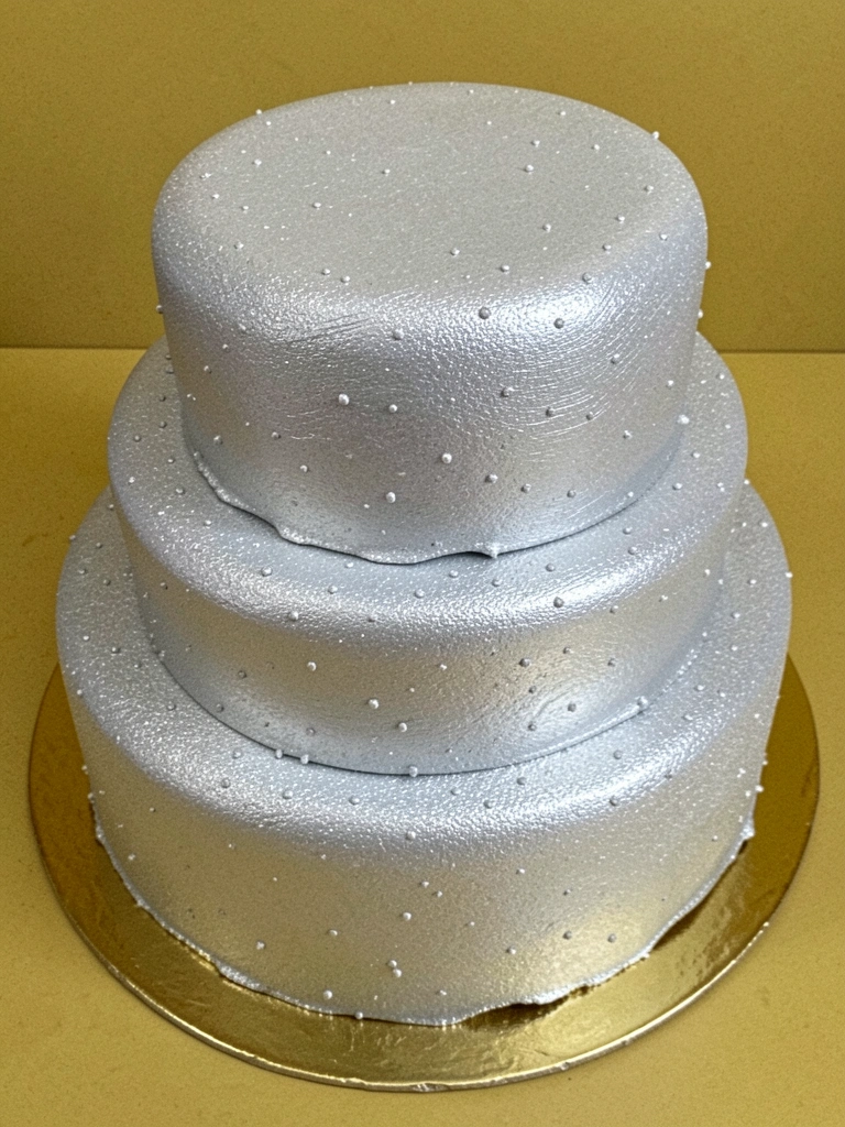 Close-up de bolo de casamento de três andares sobre base dourada com detalhes em laminado.