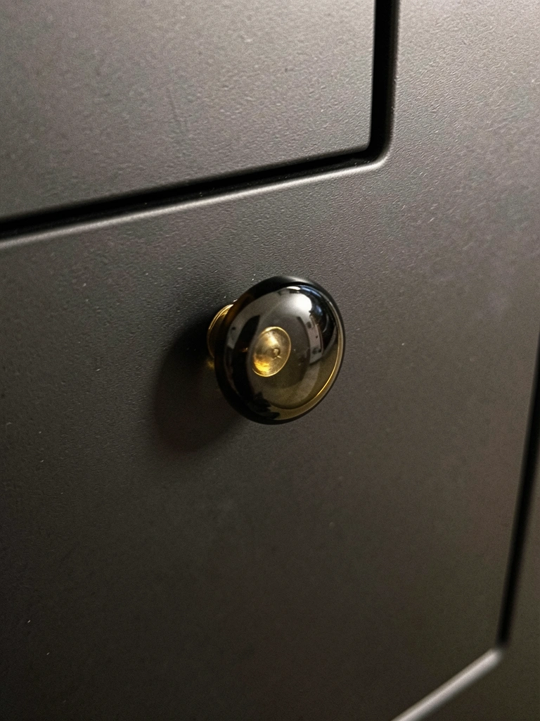 Puxador de vidro fumê com detalhe dourado em armário preto fosco, iluminado dramaticamente.