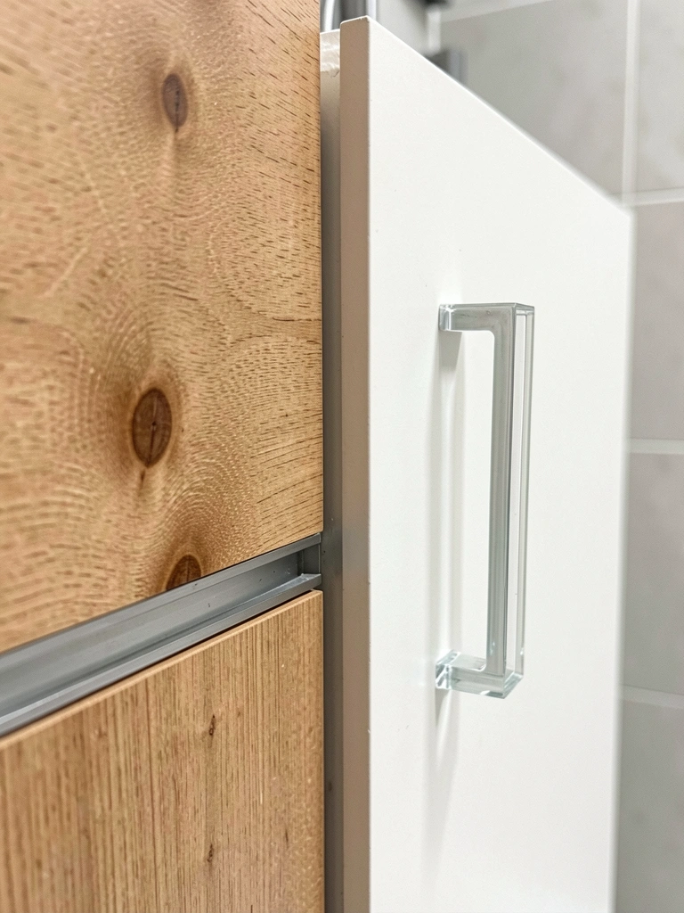 Puxador de vidro transparente em armário de banheiro com azulejos claros e toalhas.