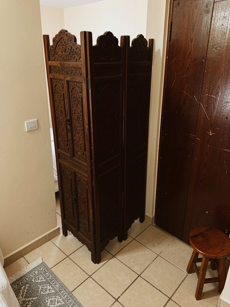 Quarto com biombo de madeira maciça fechado à frente, cama ao fundo e luz indireta.