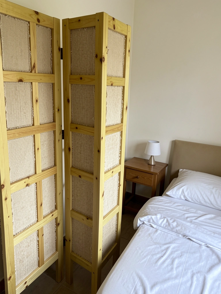 Quarto pequeno com biombo de duas folhas de madeira ao lado da cama de solteiro e mesa de cabeceira.